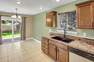 Kitchen featuring dishwashing machine, light tile patterned flooring, hanging light fixtures, stone countertops, and a chandelier