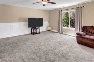 Living area featuring ceiling fan, carpet, and a wainscoted wall