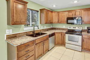Kitchen with appliances with stainless steel finishes, light tile patterned floors, and brown cabinets