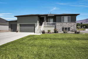 Prairie-style house featuring stone siding, an attached garage, a front lawn, concrete driveway, and stairway