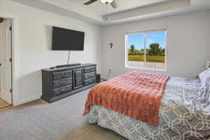 Carpeted bedroom with a raised ceiling and a ceiling fan