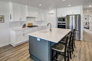 Kitchen featuring appliances with stainless steel finishes, white cabinetry, light wood-style floors, a kitchen breakfast bar, and recessed lighting