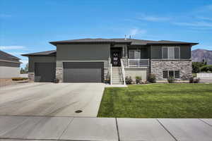 Prairie-style house featuring stone siding, a garage, a front lawn, driveway, and a mountain view