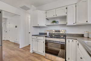 Kitchen with stainless steel range with electric cooktop, white cabinetry, dark countertops, light wood-type flooring, and open shelves