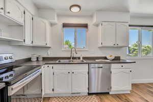 Kitchen featuring appliances with stainless steel finishes, dark countertops, white cabinets, and light wood-style flooring