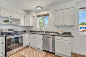 Kitchen featuring stainless steel appliances, dark countertops, white cabinetry, and light wood-style floors