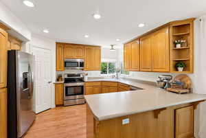 Kitchen featuring stainless steel appliances, a peninsula, open shelves, light wood-style floors, and recessed lighting
