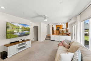 Living area featuring light colored carpet, stairs, a ceiling fan, and recessed lighting