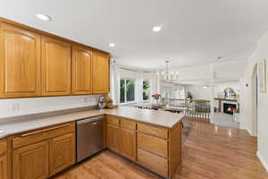 Kitchen with stainless steel dishwasher, a peninsula, light countertops, light wood-style flooring, and recessed lighting