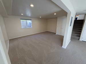 Basement featuring a textured ceiling, light colored carpet, recessed lighting, and stairs