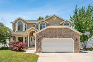 Traditional home with an attached garage, driveway, a front lawn, stucco siding, and brick siding