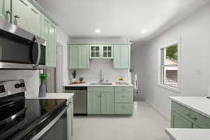Kitchen featuring green cabinets, appliances with stainless steel finishes, light countertops, recessed lighting, and glass insert cabinets