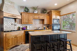 Kitchen featuring black appliances, custom exhaust hood, a kitchen island, backsplash, and recessed lighting