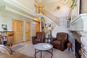 Living area featuring stairway, a stone fireplace, a towering ceiling, and a chandelier