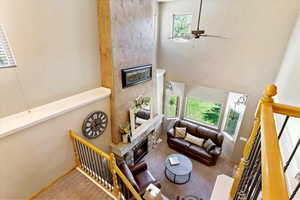 Living area featuring a large fireplace, carpet flooring, ceiling fan, and a towering ceiling