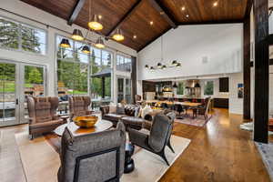 Living area with a wooden ceiling with exposed beams, high vaulted ceiling, wood finished floors, a chandelier, and french doors