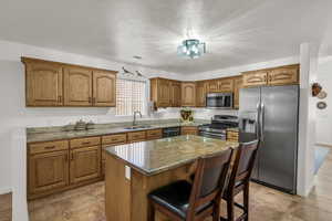 Kitchen featuring dark stone countertops, stainless steel appliances, a kitchen breakfast bar, a kitchen island, and brown cabinets