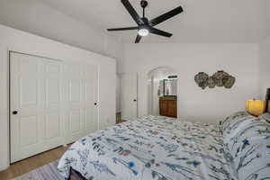 Bedroom featuring lofted ceiling, a closet, wood finished floors, arched walkways, and ceiling fan