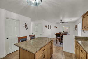 Kitchen featuring a ceiling fan, a kitchen island, light tile patterned flooring, dark stone counters, and a textured ceiling