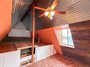 Additional living space with a textured wall, wood walls, and ceiling fan