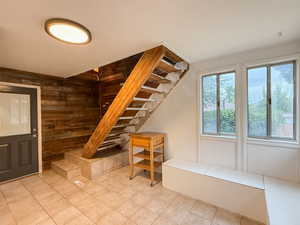 Entryway featuring wooden walls, light tile patterned flooring, and stairway
