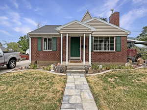 Bungalow with brick siding, a chimney, a front yard, and driveway