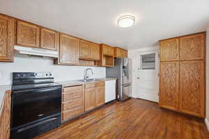Kitchen with black range with electric stovetop, dark wood-type flooring, under cabinet range hood, light countertops, and white dishwasher