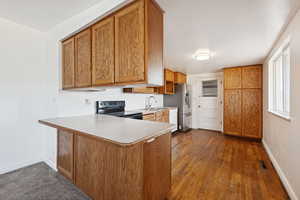 Kitchen with brown cabinetry, a peninsula, black electric range, light countertops, and dark wood-style flooring
