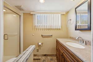 Full bath with vanity, a shower stall, plenty of natural light, and light stone finish floors