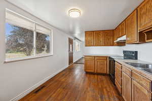 Kitchen with black range with electric cooktop, dark wood finished floors, light countertops, brown cabinets, and under cabinet range hood