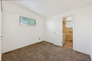Unfurnished bedroom with dark colored carpet, lofted ceiling, and connected bathroom