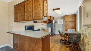 Kitchen with black range with electric cooktop, brown cabinetry, stainless steel refrigerator with ice dispenser, and a peninsula
