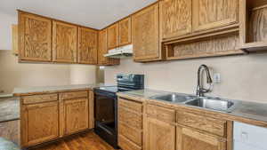Kitchen with under cabinet range hood, black range with electric stovetop, dark wood-style flooring, light countertops, and a peninsula