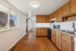 Kitchen with black range with electric stovetop, dark wood-style flooring, brown cabinets, and light countertops