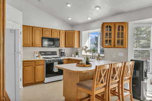 Kitchen featuring white appliances, vaulted ceiling, a peninsula, a kitchen breakfast bar, and glass insert cabinets