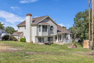 Rear view of house with a storage shed, roof with shingles, a yard, and a chimney