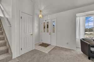 Carpeted entrance foyer featuring stairway, a chandelier, and tile patterned flooring