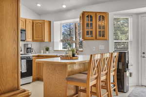Kitchen featuring gas range, black microwave, glass insert cabinets, a peninsula, and light countertops