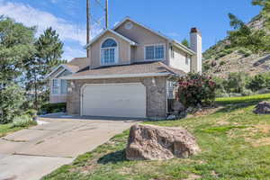 Traditional-style house with a chimney, concrete driveway, a front lawn, and brick siding