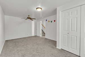 Carpeted spare room featuring stairway and a ceiling fan