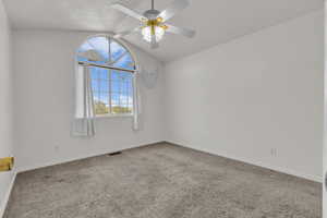 Carpeted spare room featuring vaulted ceiling and ceiling fan
