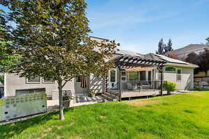 Rear view of property with a pergola, stucco siding, roof mounted solar panels, a lawn, and a deck
