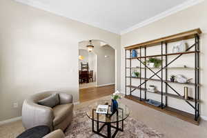 Living area with arched walkways, crown molding, and carpet floors