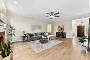 Living area with arched walkways, baseboard heating, a ceiling fan, light wood-type flooring, and ornamental molding