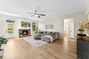 Living area with a ceiling fan, ornamental molding, light wood finished floors, and a brick fireplace