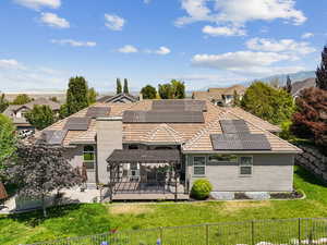 Rear view of house with a fenced backyard, stucco siding, solar panels, a wooden deck, and a tile roof