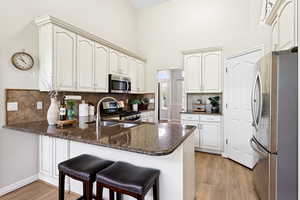 Kitchen with stainless steel appliances, a peninsula, light wood finished floors, decorative backsplash, and dark stone counters