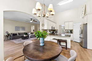 Dining room featuring ceiling fan, a towering ceiling, a chandelier, light wood-style floors, and arched walkways