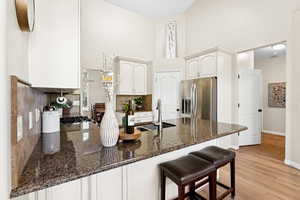 Kitchen featuring stainless steel fridge with ice dispenser, a peninsula, a towering ceiling, decorative backsplash, and dark stone counters