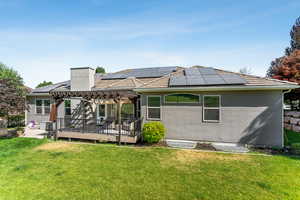 Rear view of property with a pergola, roof mounted solar panels, a yard, a chimney, and stucco siding
